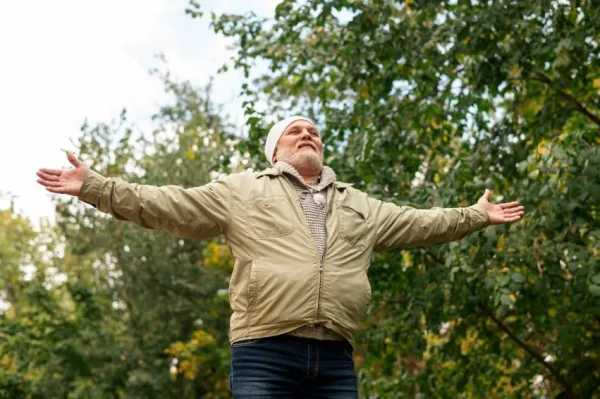 A senior man spreading his arms in joy and embracing the outdoors, symbolizing the relief provided by Oxeze asthma medication.